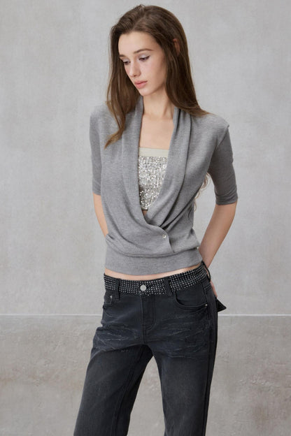Woman wearing a gray cardigan over a sequined top and black pants against a plain background