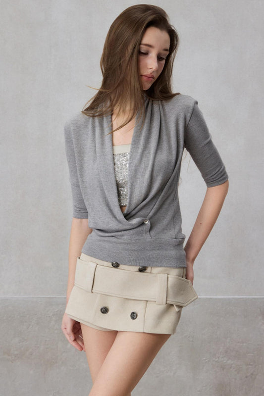 Woman wearing a gray cardigan over a patterned top and beige skirt against a plain background