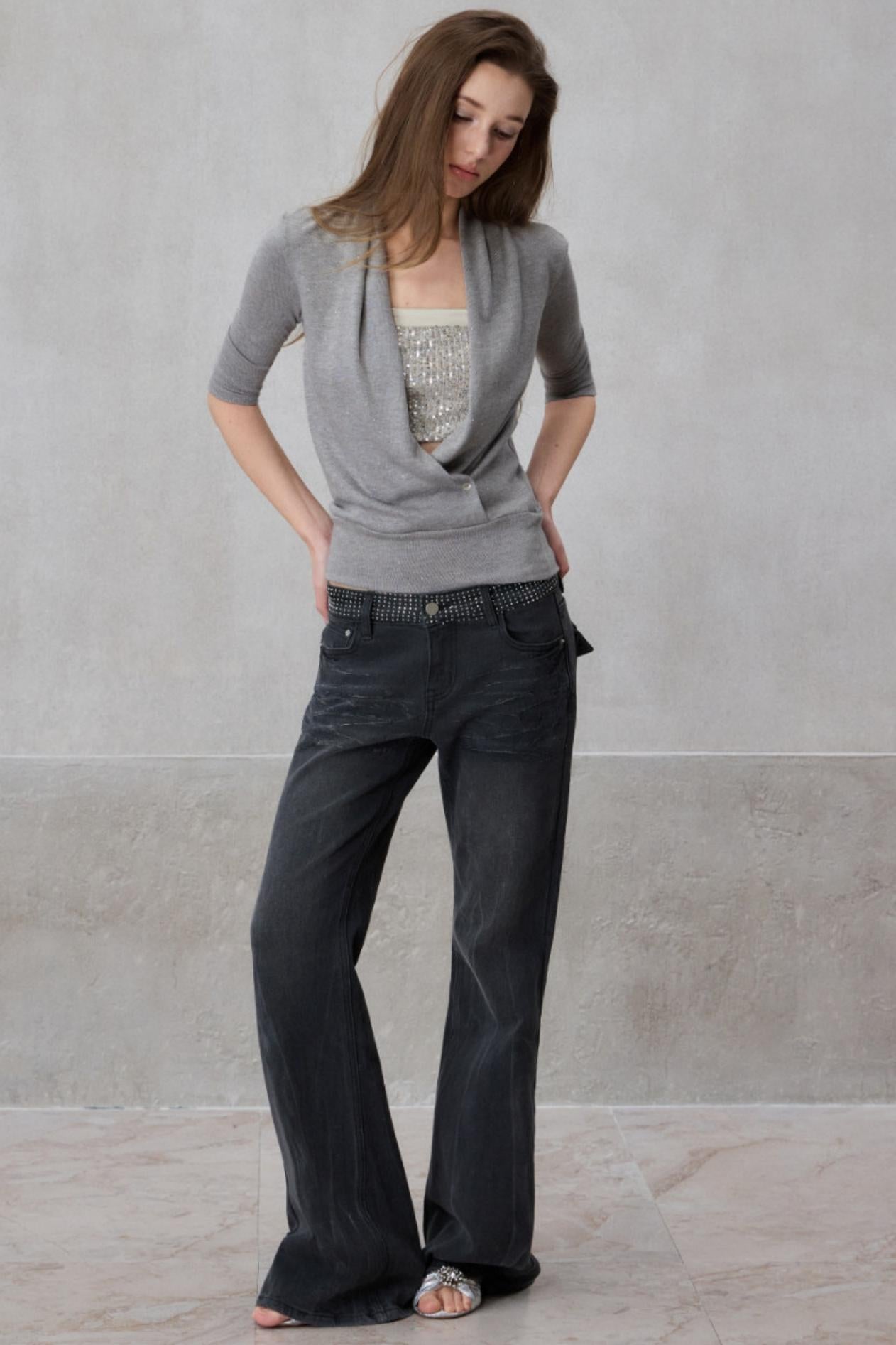 Woman wearing a gray cardigan and dark jeans against a plain background