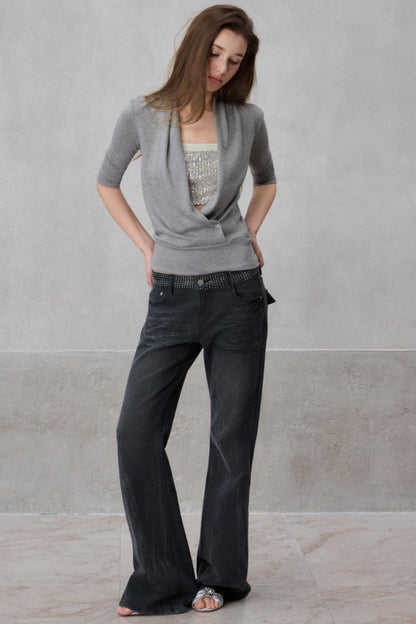 Woman wearing a gray cardigan and dark jeans against a plain background