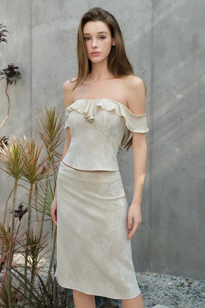 Woman wearing a light-colored off-shoulder top and skirt against a gray wall.