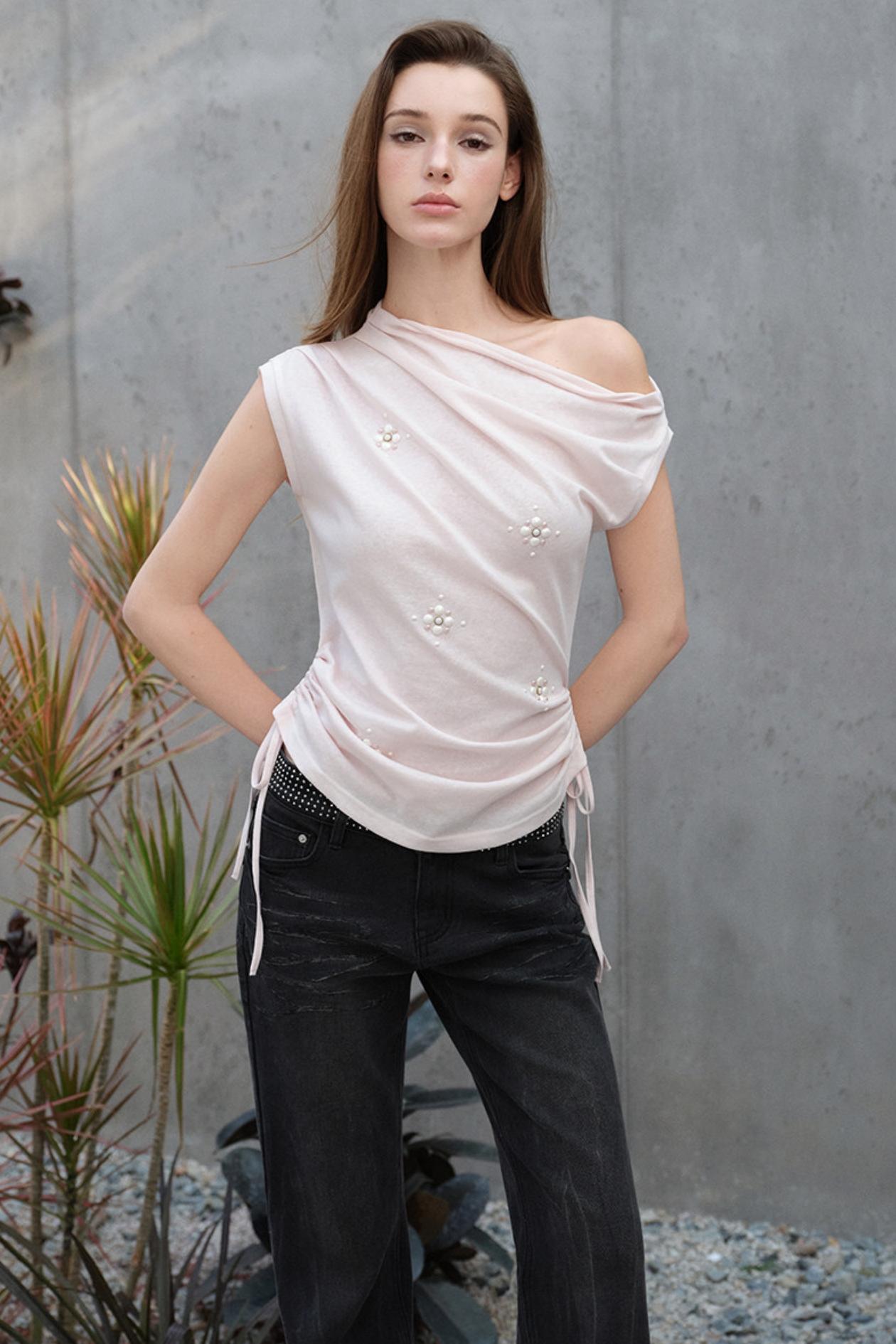 Woman wearing a white off-shoulder top with black pants against a gray wall.