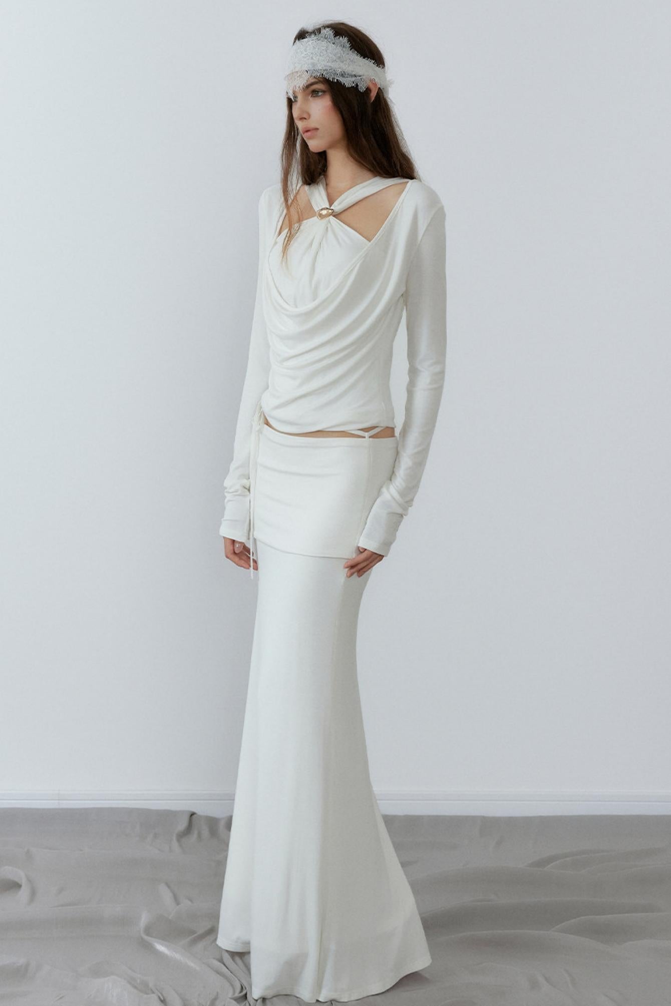 Woman wearing a long-sleeve white dress with a fitted skirt against a plain background