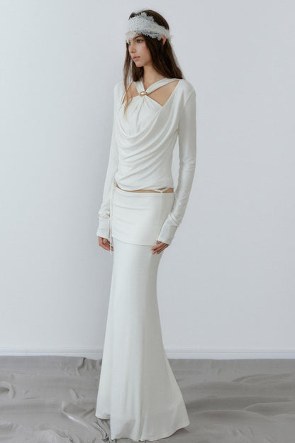 Woman wearing a long-sleeve white dress with a fitted skirt against a plain background