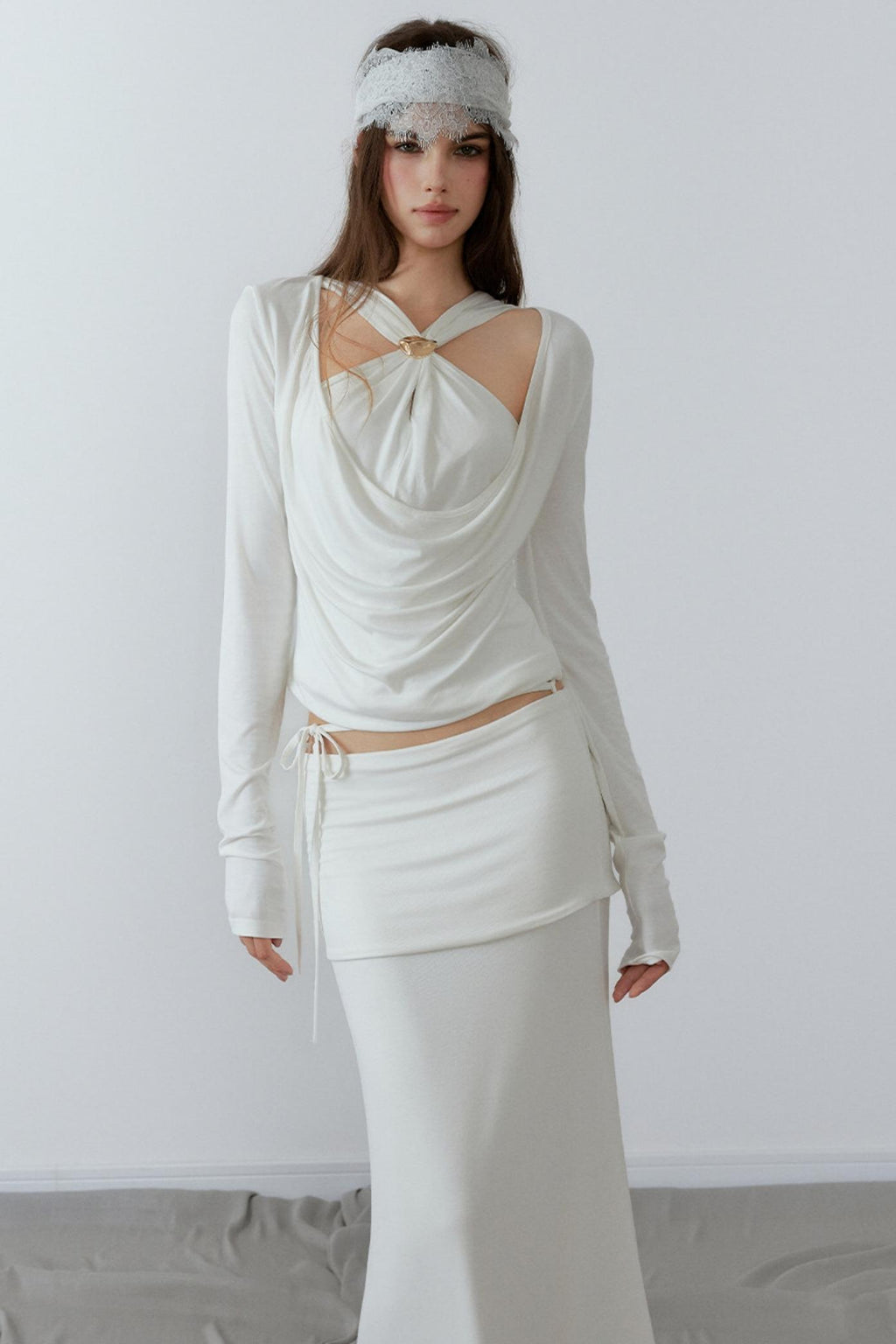 Model showcasing a chic cream long sleeve fake two-piece top featuring a draped cowl neck, halter straps, and a sleek metal knot detail.