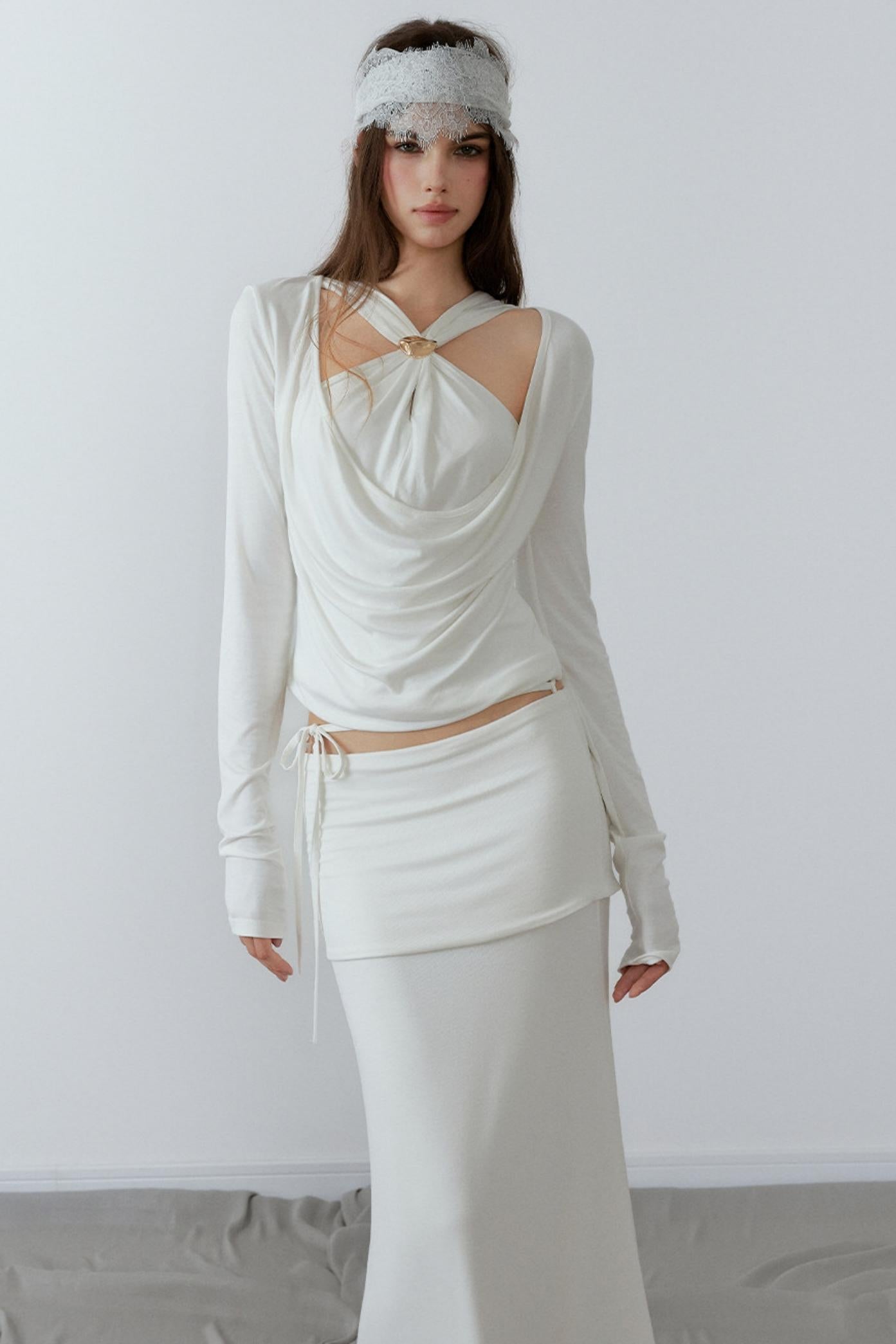 Model showcasing a chic cream long sleeve fake two-piece top featuring a draped cowl neck, halter straps, and a sleek metal knot detail.