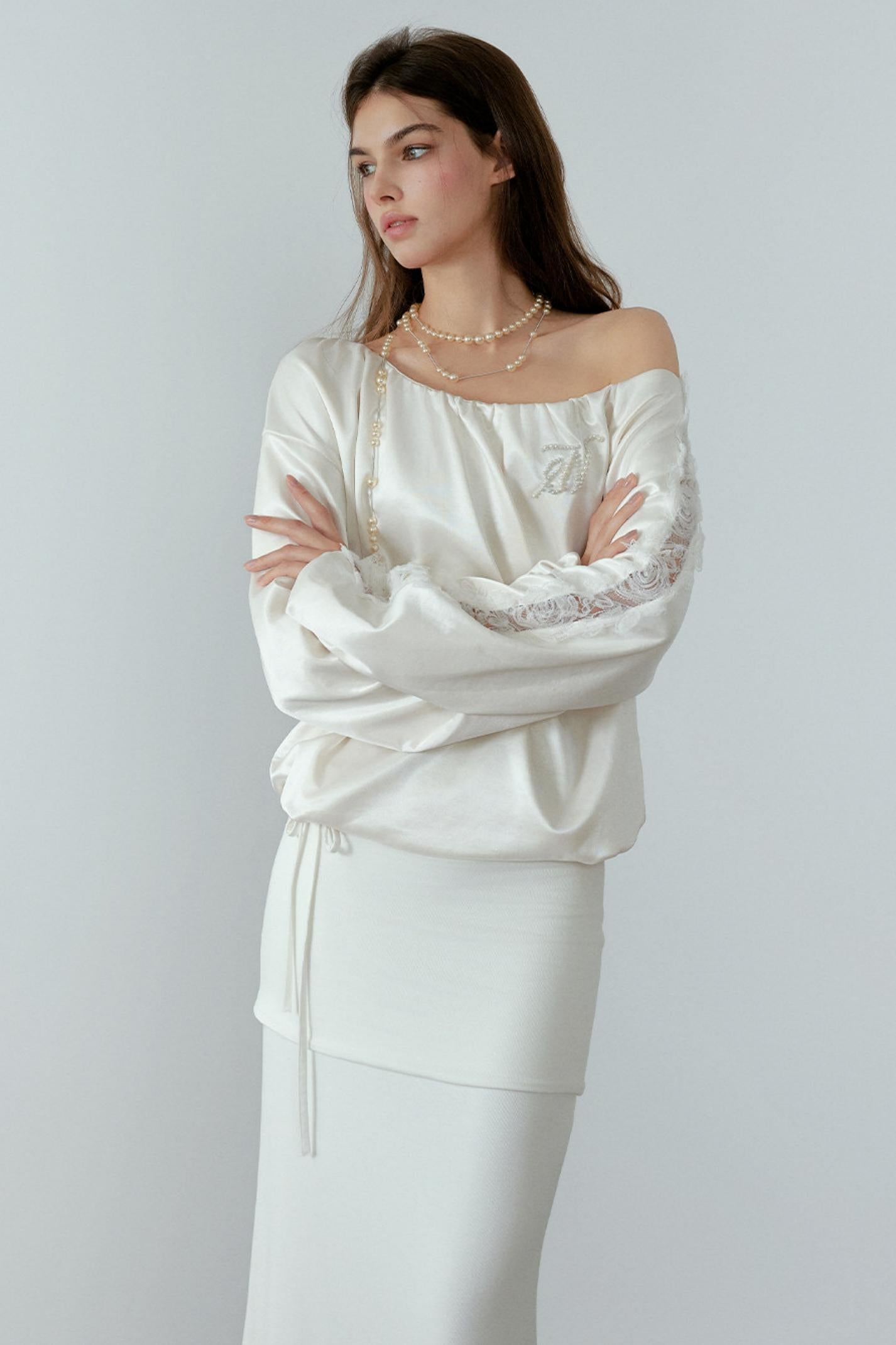 Woman wearing a white off-shoulder top with lace details on a plain background
