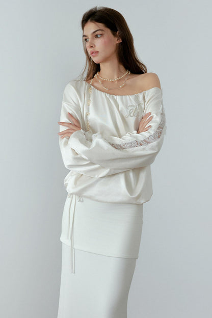 Woman wearing a white off-shoulder top with lace details on a plain background