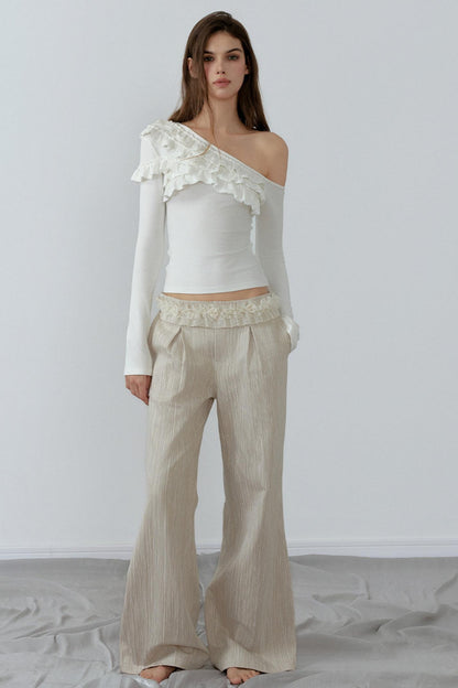 Woman wearing a white off-shoulder top with lace details and beige pants on a plain background