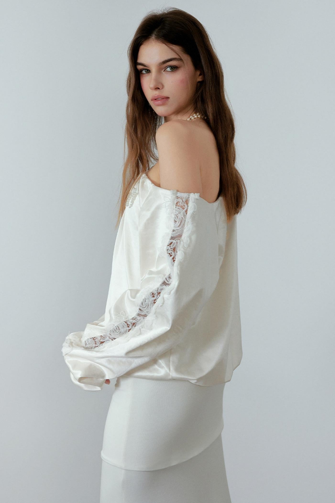 Woman wearing a white satin top with lace details on a plain background