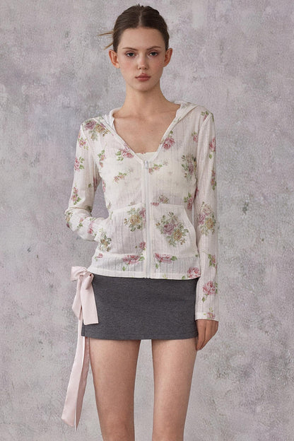 Model wearing a slim-fit floral print pointelle knit hooded cardigan with ribbon details, paired with a dark mini skirt.
