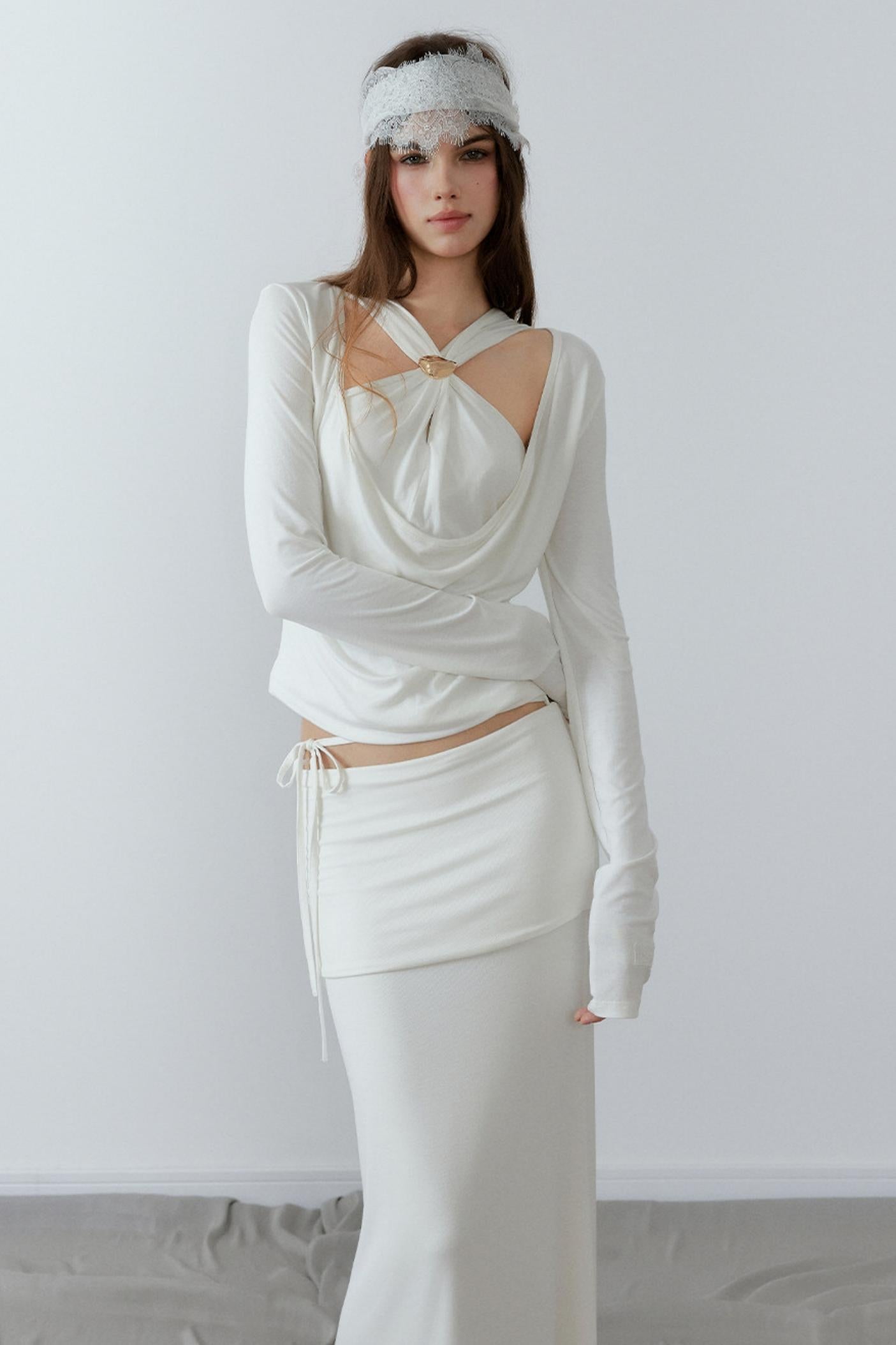Model showcasing a chic cream long sleeve fake two-piece top featuring a draped cowl neck, halter straps, and a sleek metal knot detail.