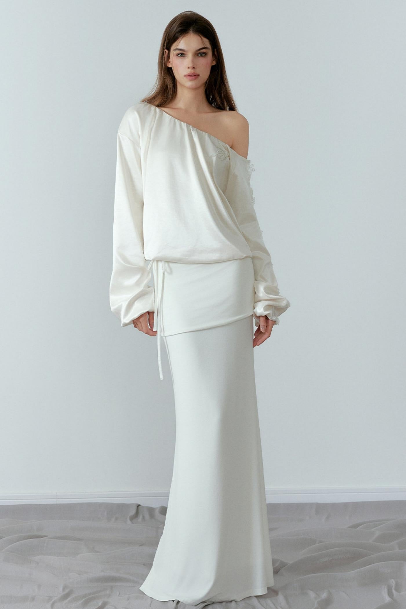 Woman wearing a white one-shoulder top and skirt set against a plain background