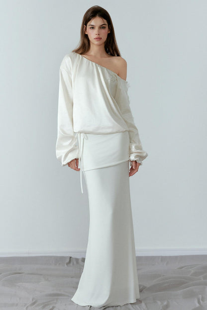 Woman wearing a white one-shoulder top and skirt set against a plain background