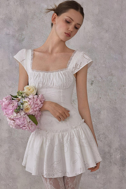 Woman in a white lace dress holding flowers against a gray background