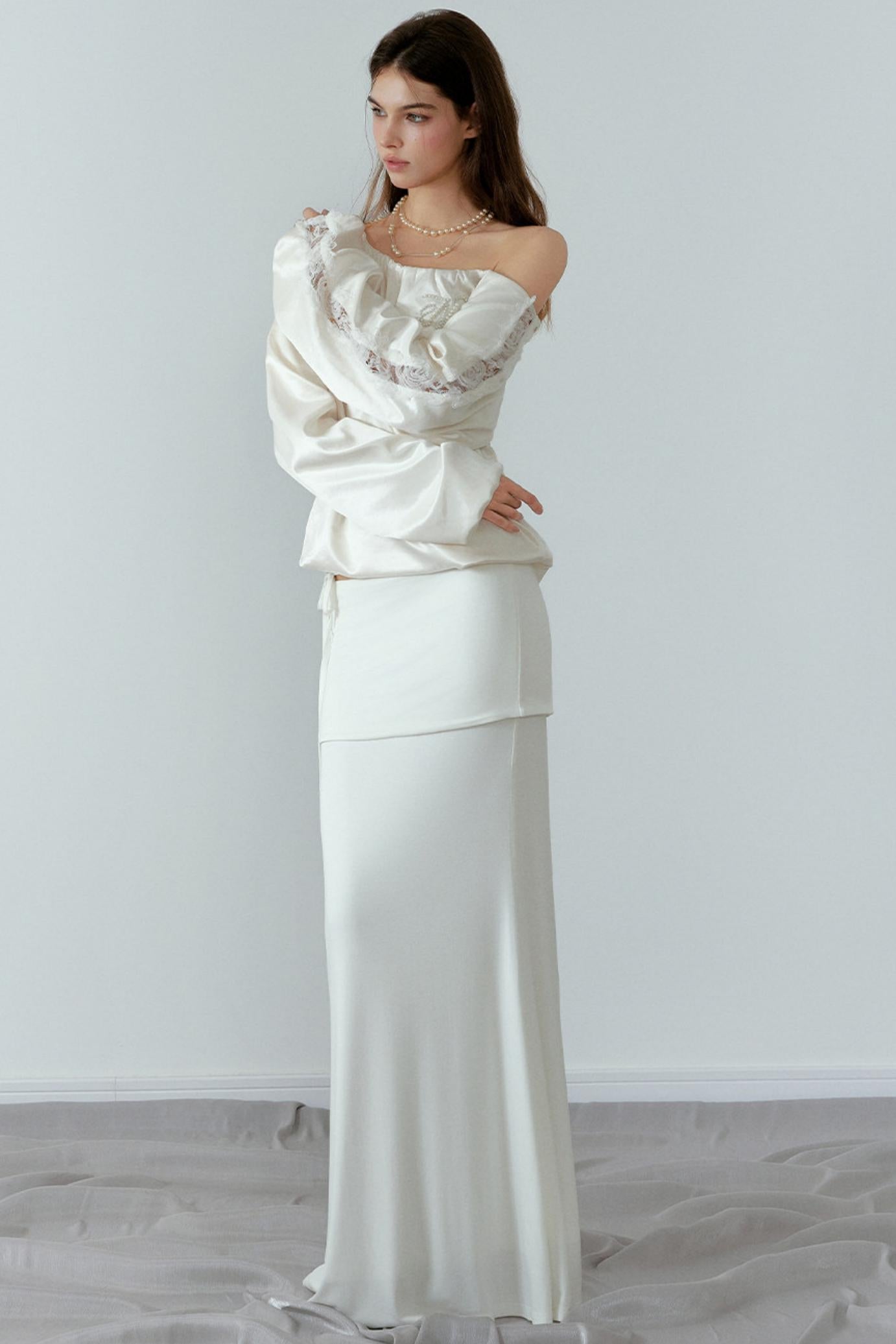 Woman wearing a white off-shoulder top and long skirt against a plain background