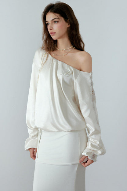 Woman wearing a white off-shoulder top and white pants against a plain background