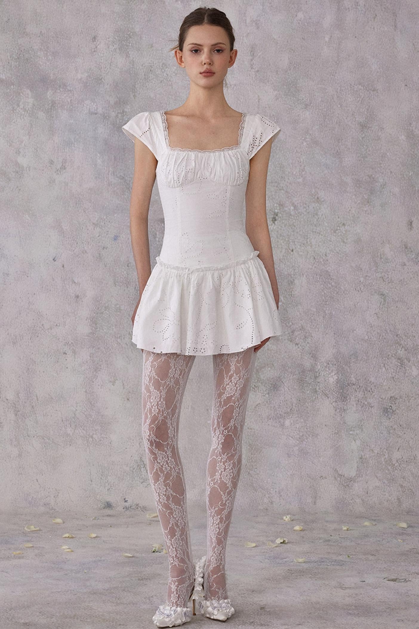 Model wearing a white dress with sheer tights against a gray background