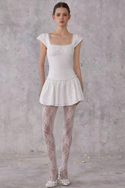 Model wearing a white dress with sheer tights against a gray background
