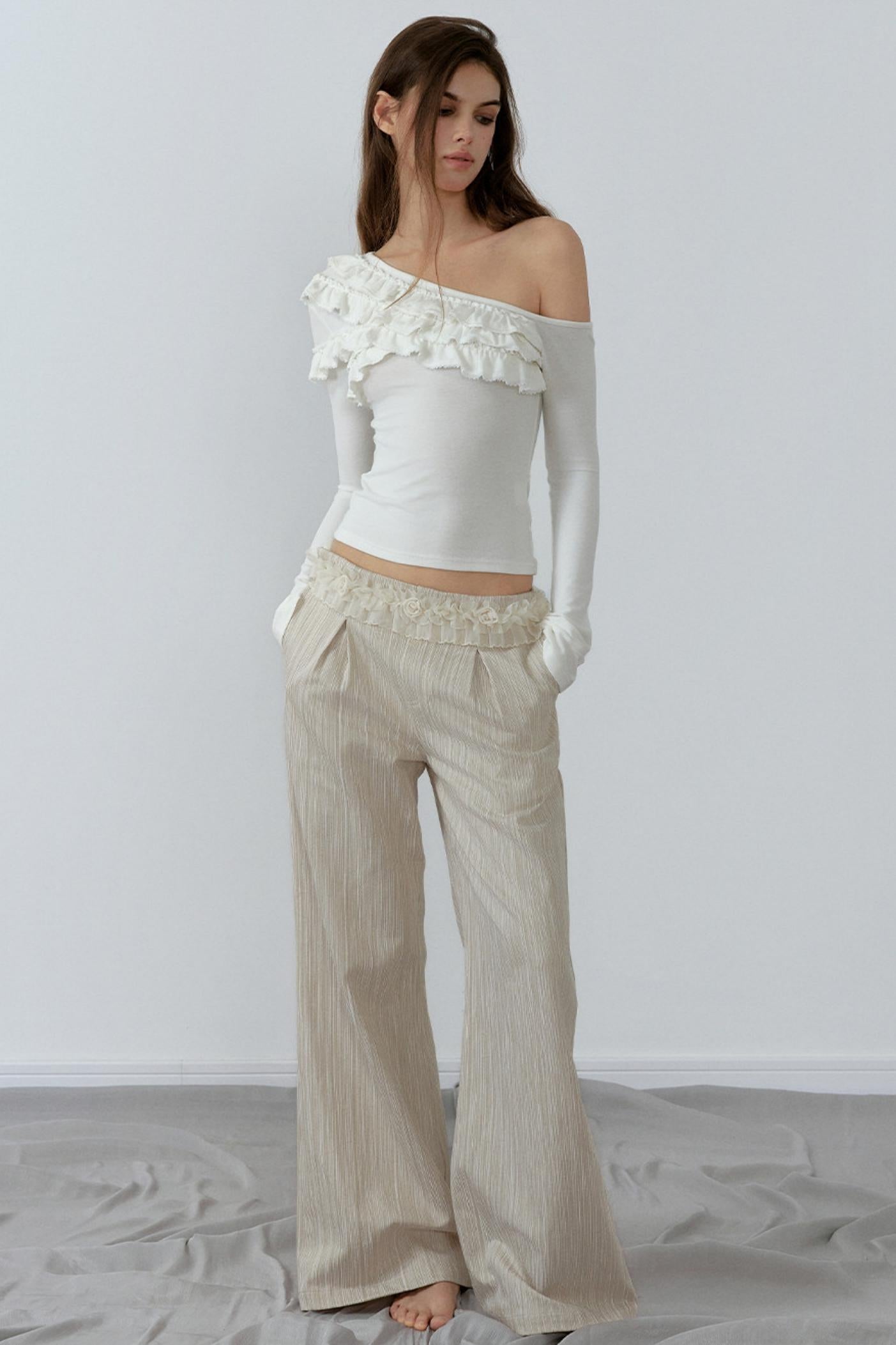 Woman wearing a white off-shoulder top and beige pants with a white background
