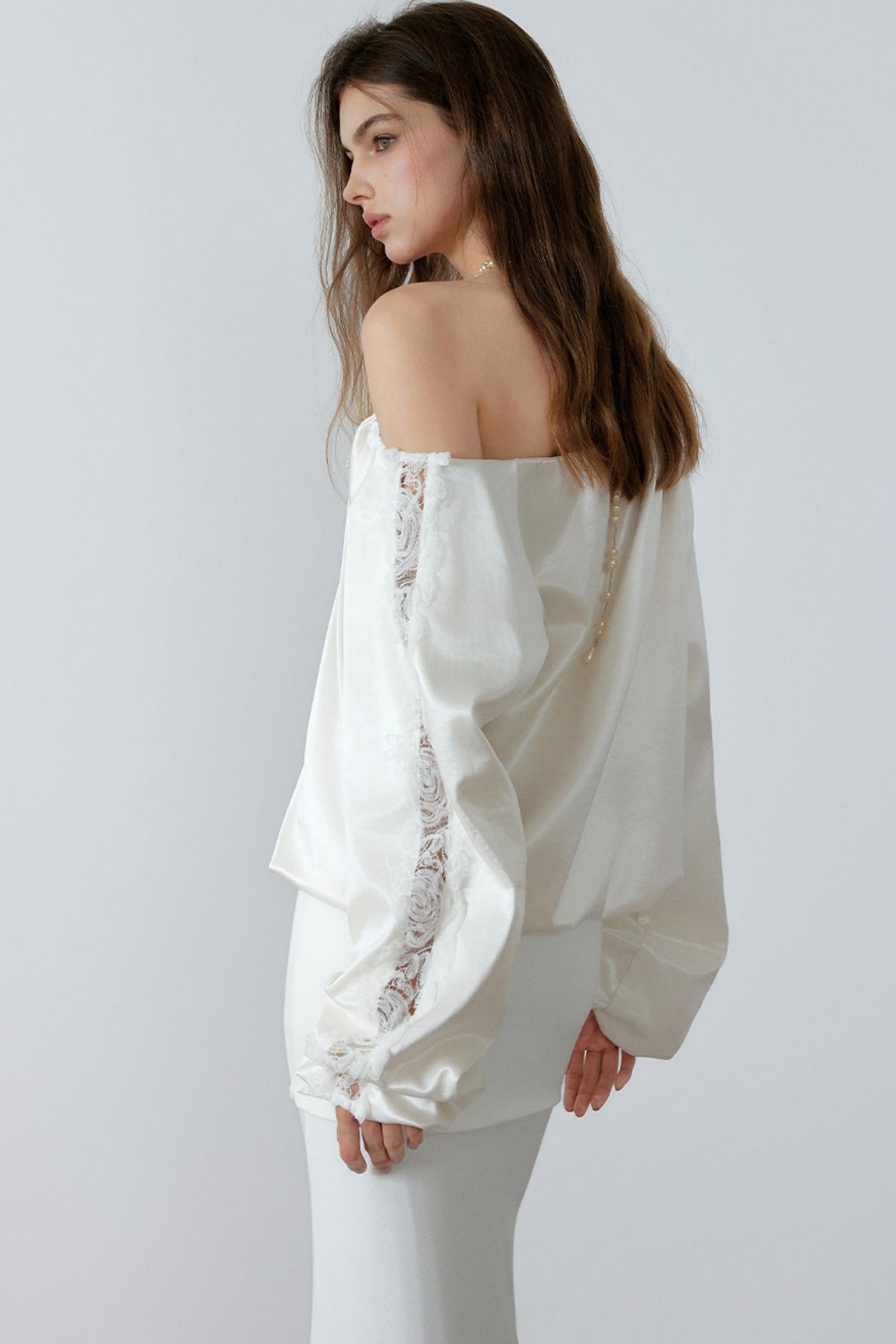 Woman wearing a white off-shoulder blouse with lace details on a plain background
