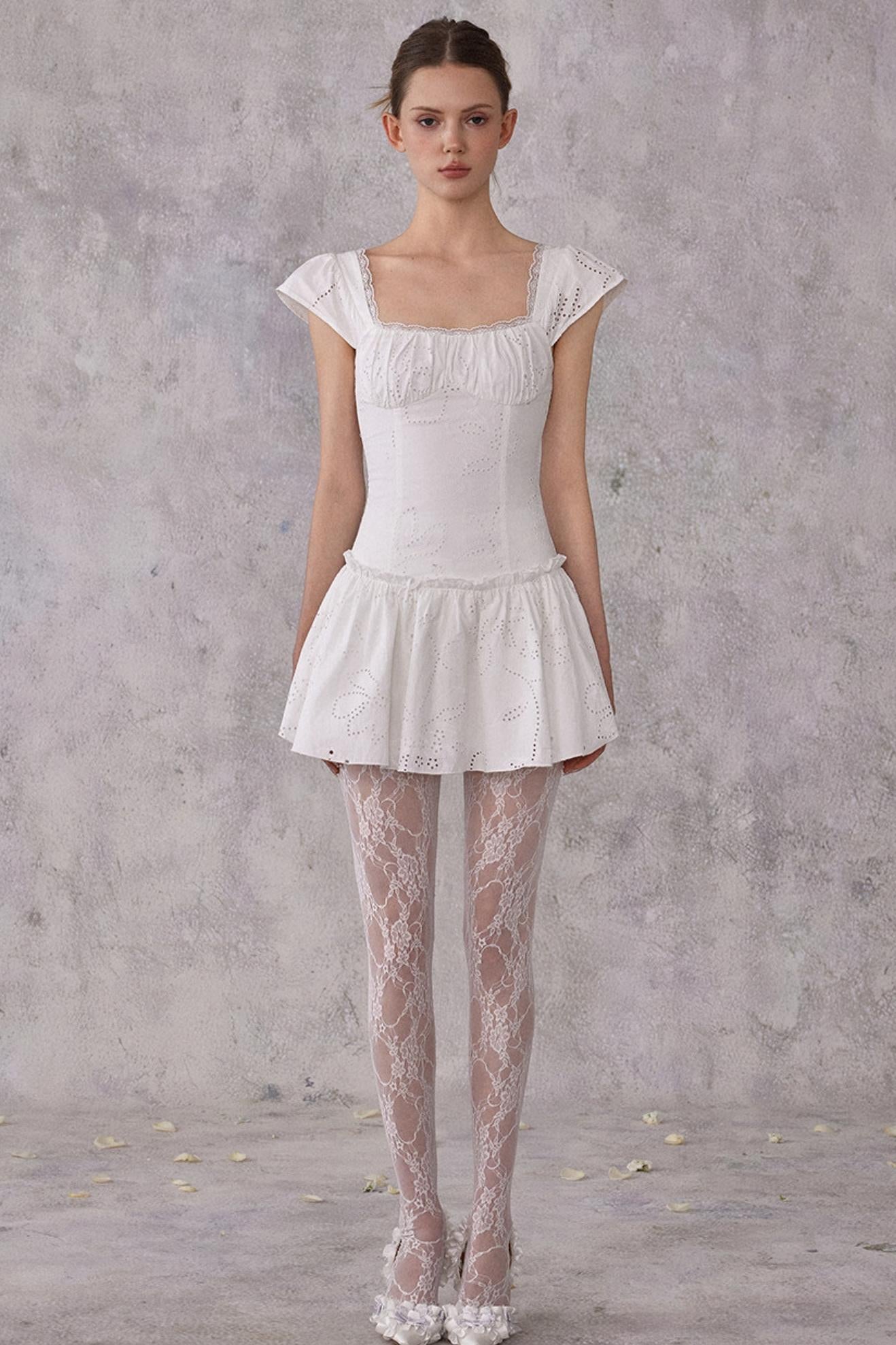 Model wearing a white lace dress and stockings against a gray background