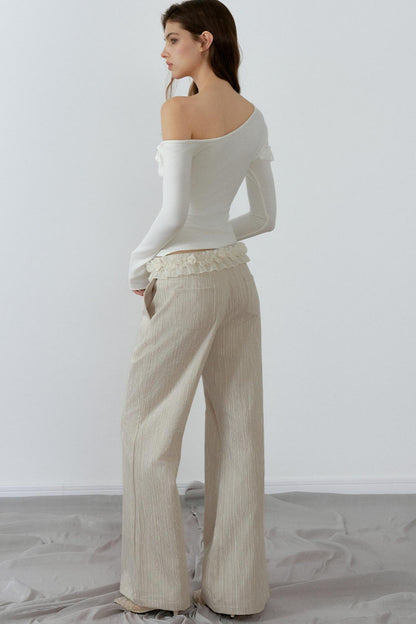 Woman wearing a white off-shoulder top and beige pants against a plain background
