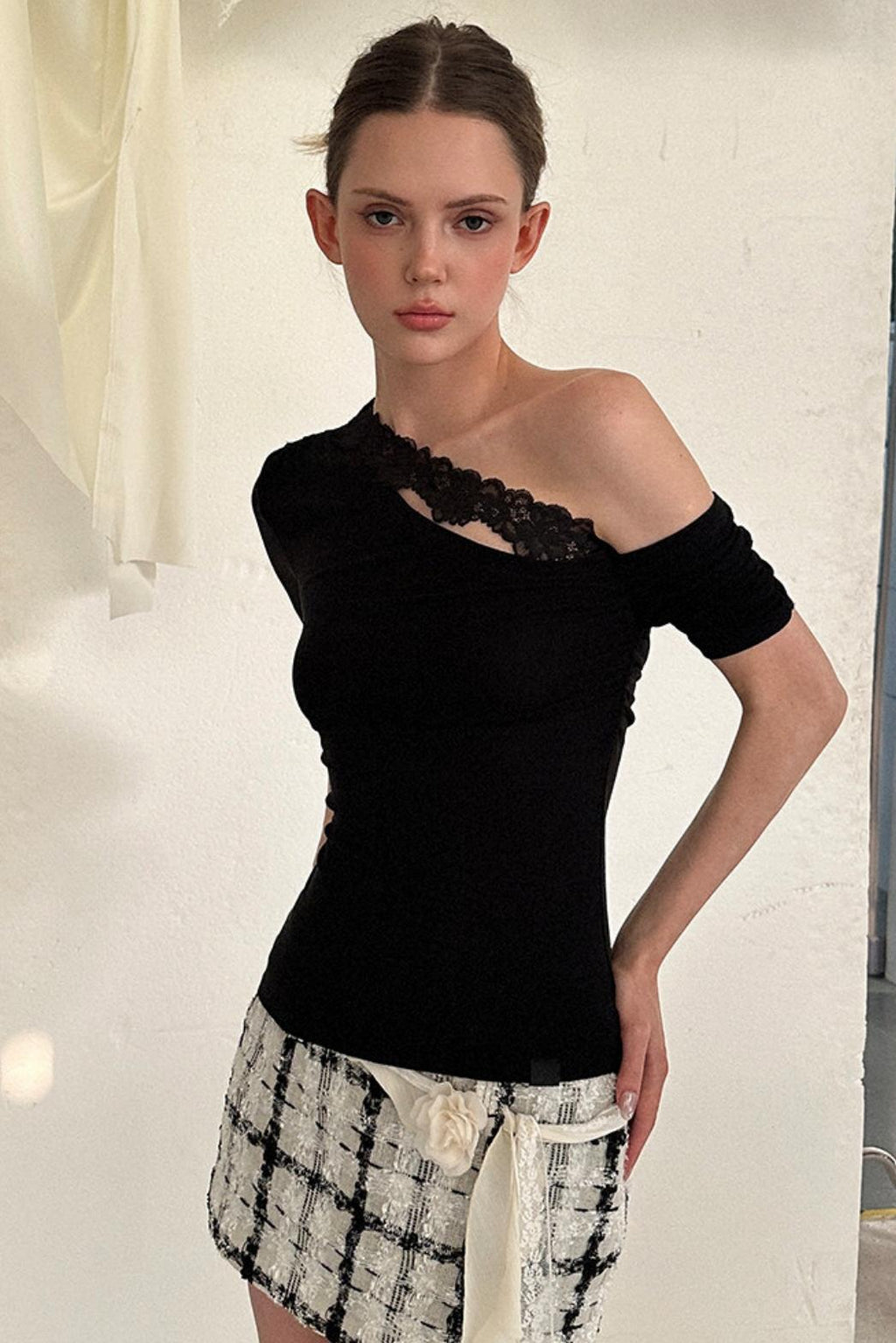 Woman wearing a black one-shoulder top with lace details and a patterned skirt.