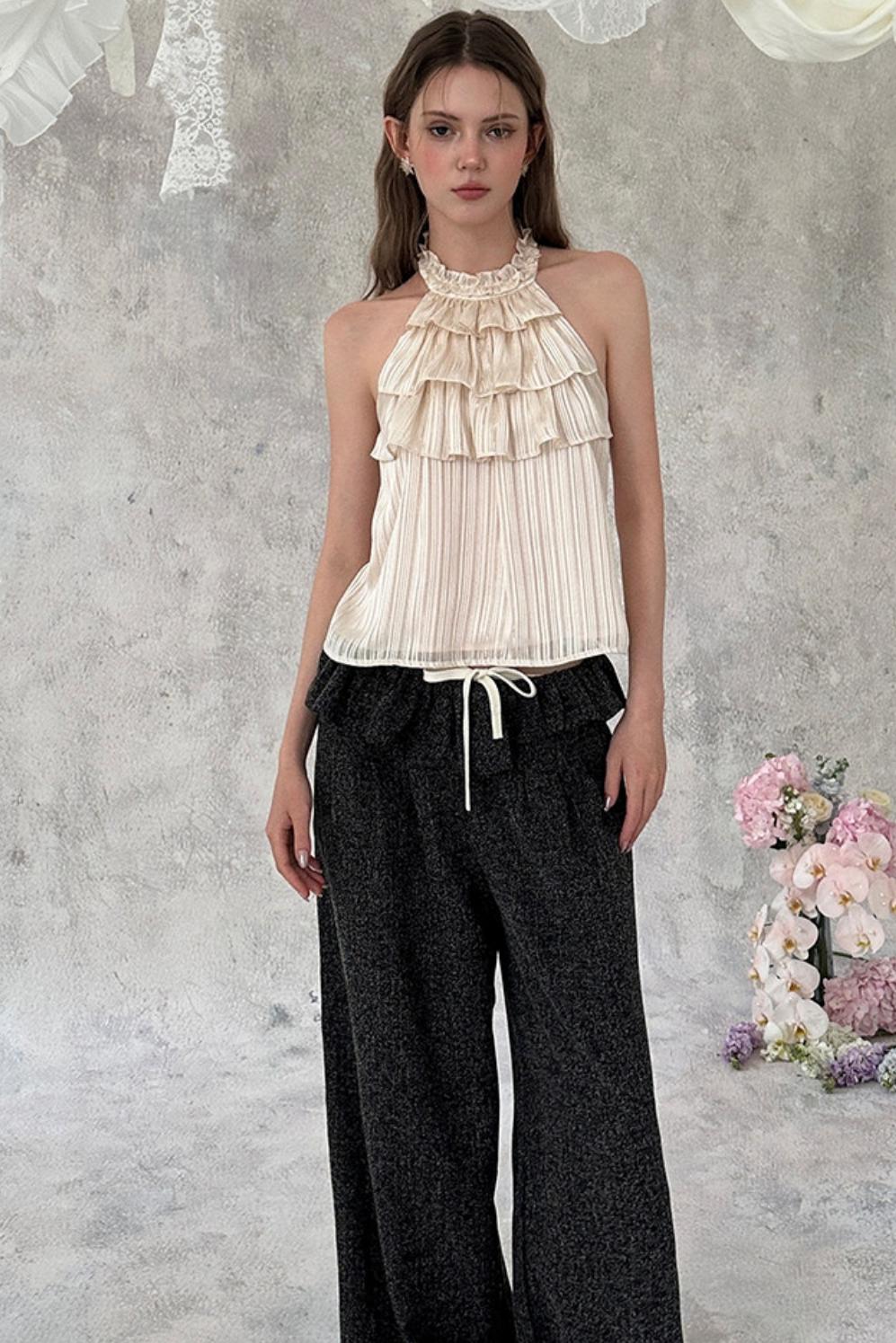Woman wearing a beige ruffled top and black pants against a gray textured background with flowers.