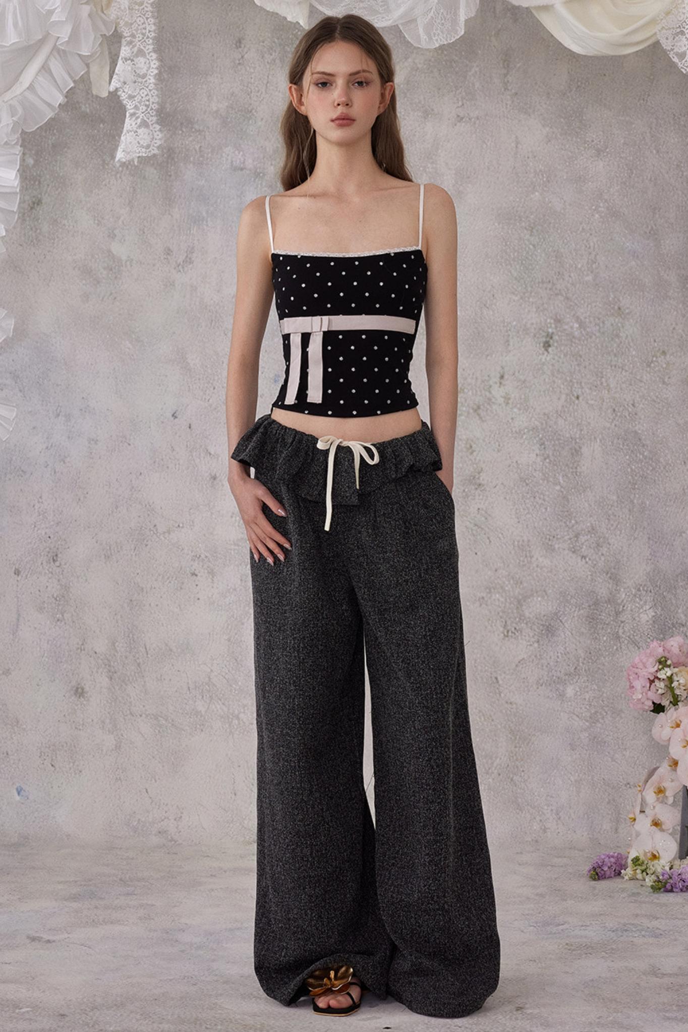 Woman wearing a black and white top and dark gray pants against a textured gray wall.