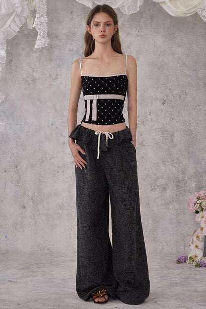Woman wearing a black and white top and dark gray pants against a textured gray wall.