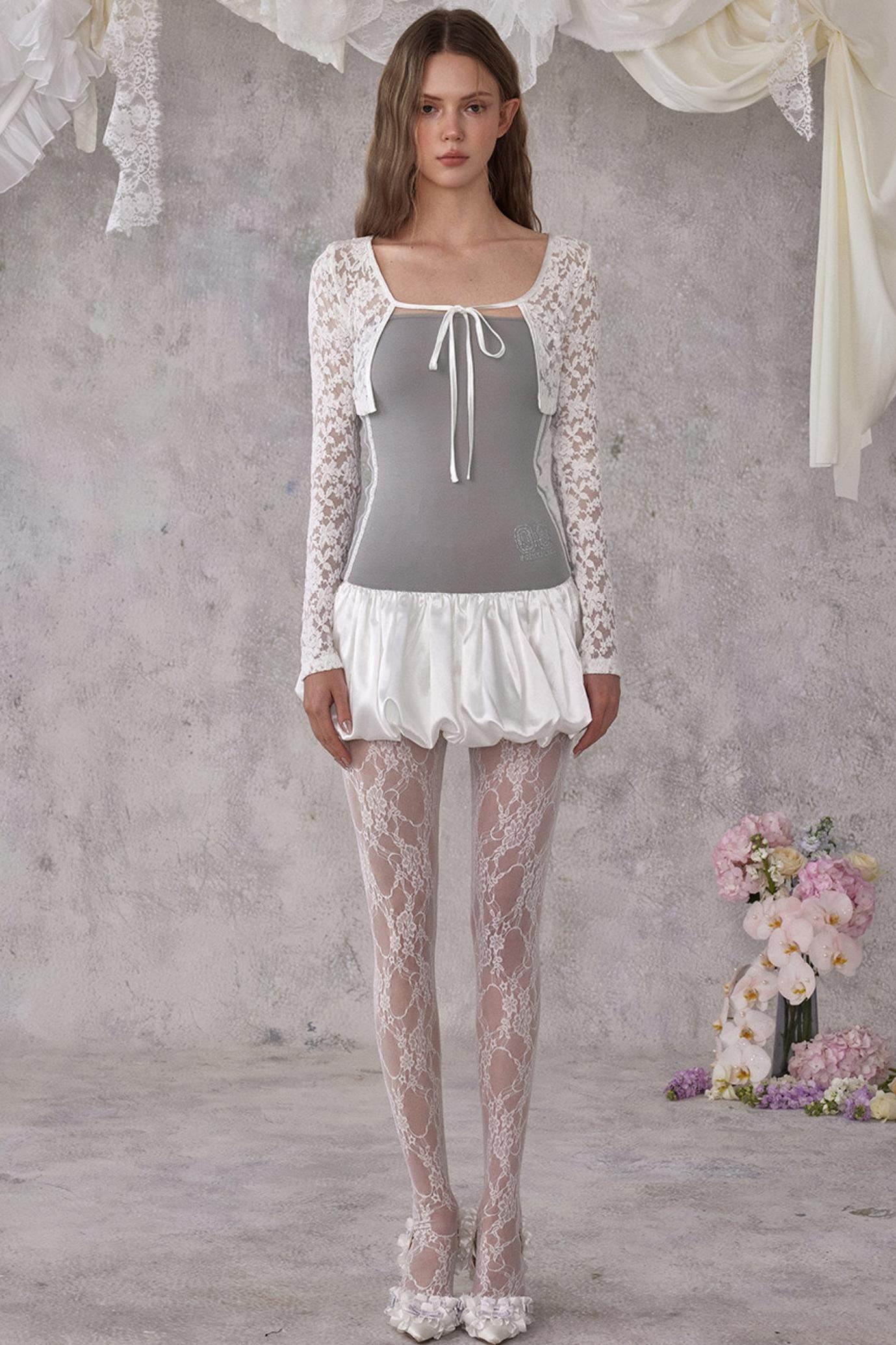 Woman wearing a lace outfit with a gray top and white skirt against a textured wall.