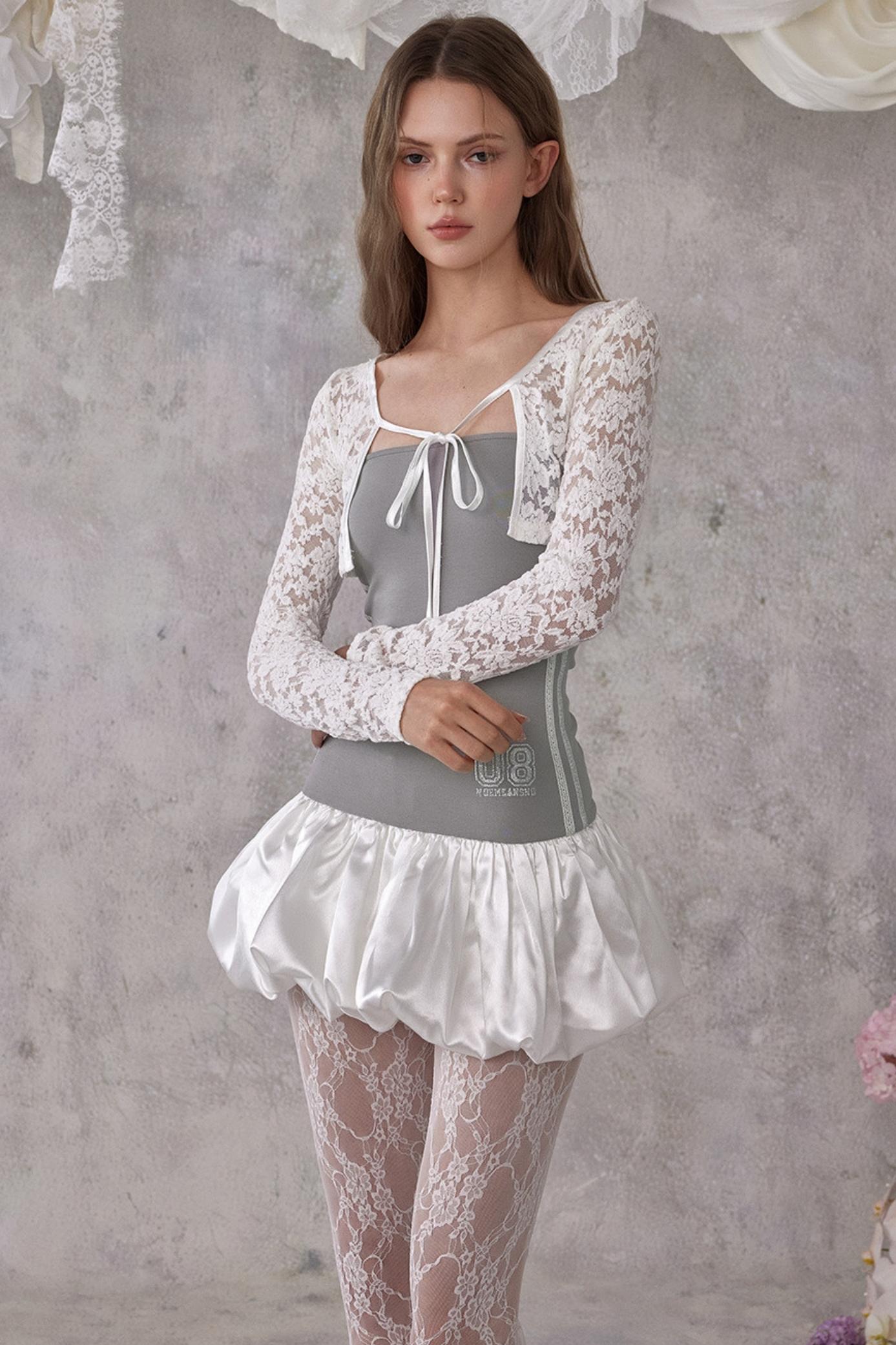 Woman wearing a lace outfit with a gray top against a textured wall.
