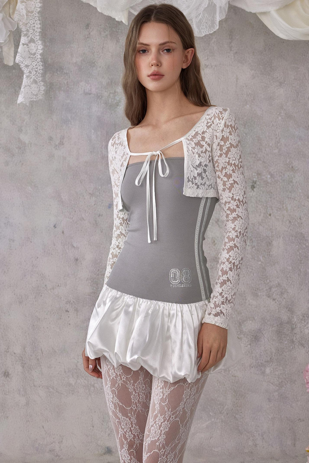 Woman wearing a gray top with lace sleeves and skirt against a textured gray wall.