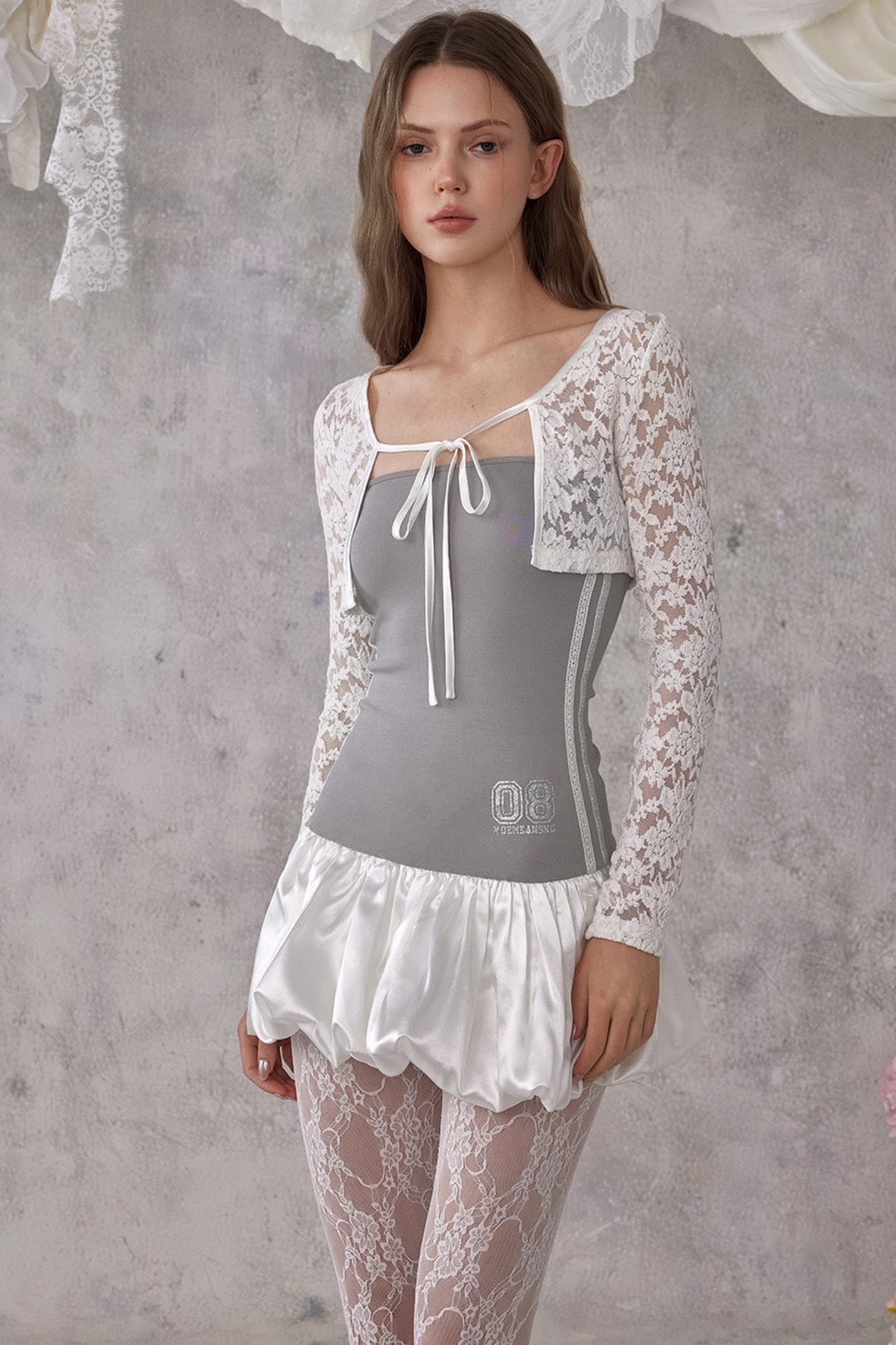 Woman wearing a gray top with lace sleeves and skirt against a textured gray wall.