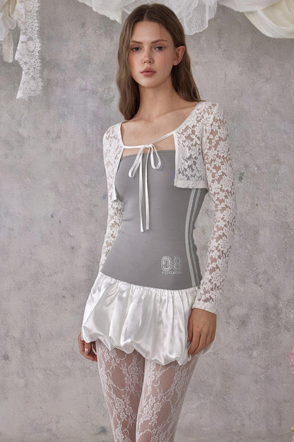Woman wearing a gray top with lace sleeves and skirt against a textured gray wall.
