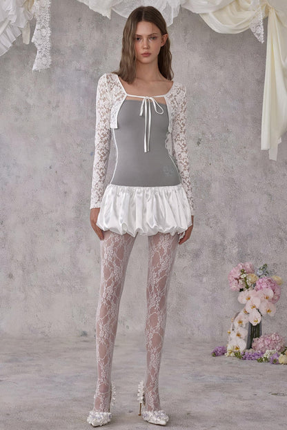 Woman wearing a lace outfit with a gray top and white skirt against a neutral background.