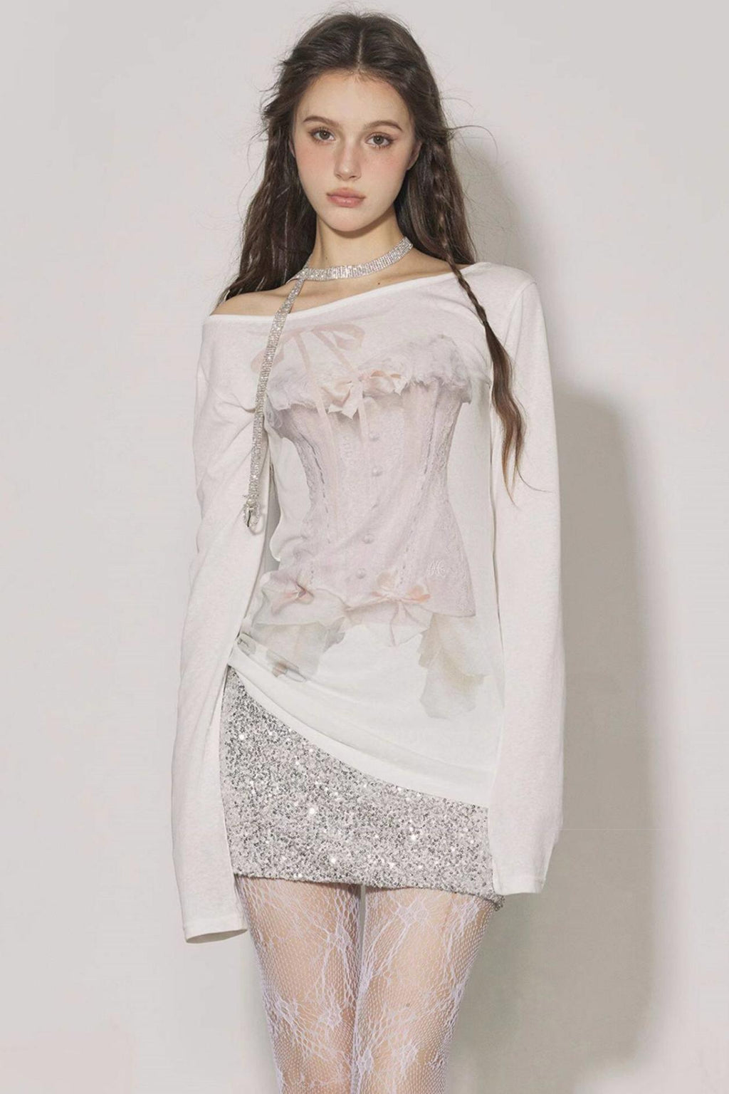 Woman wearing a light pink off-shoulder top with floral details and a silver sequin skirt on a plain background.