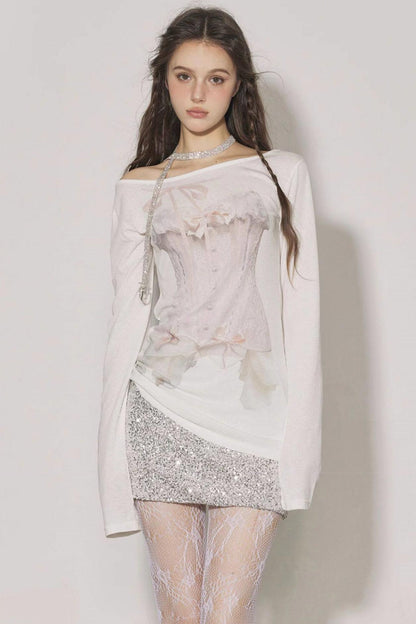 Woman wearing a light pink off-shoulder top with floral details and a silver sequin skirt on a plain background.