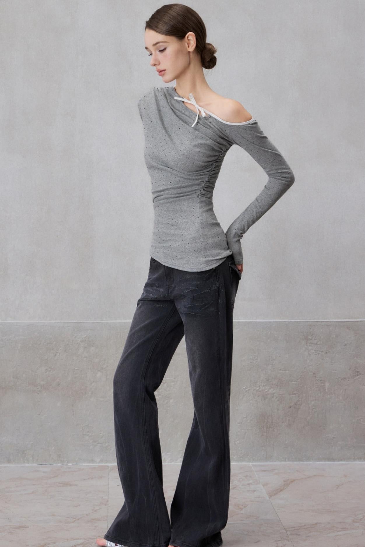 Woman wearing a gray off-shoulder top and dark pants against a plain background
