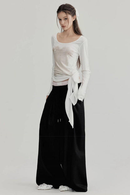 Woman wearing a white top with a bow and black pants on a light gray background