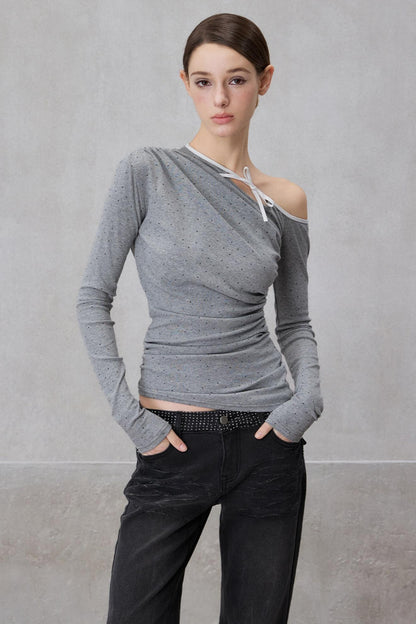 Woman wearing a gray off-shoulder top and black pants against a plain background