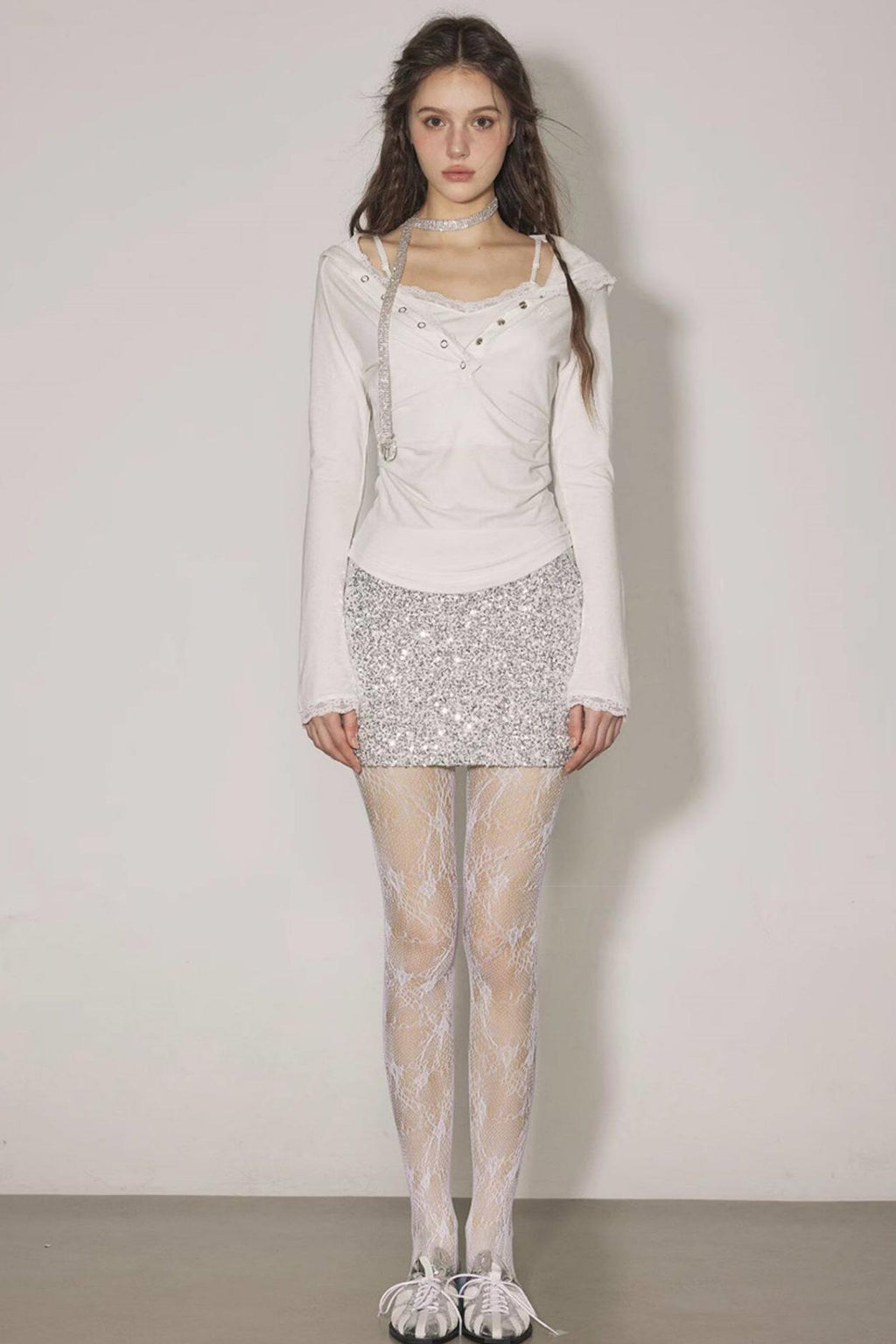 Woman wearing a white outfit with a sequined skirt against a plain background