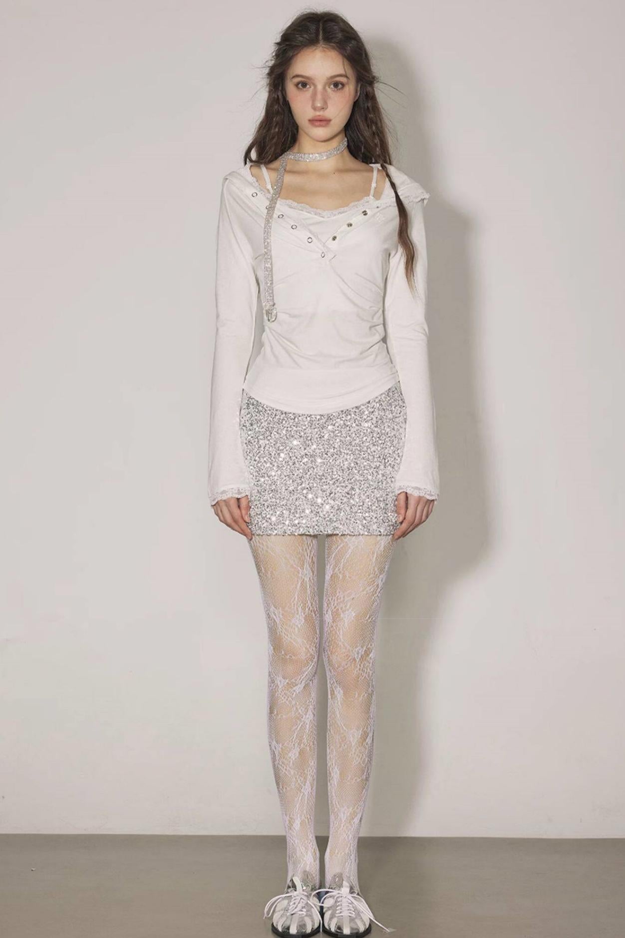 Woman wearing a white outfit with a sequined skirt against a plain background