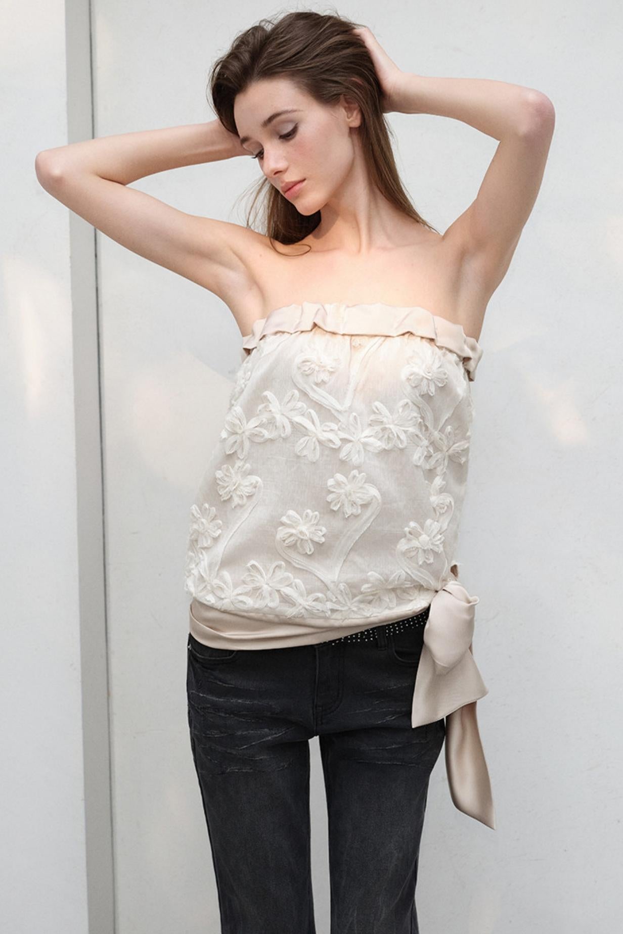 Woman wearing a white floral top and black pants against a plain background