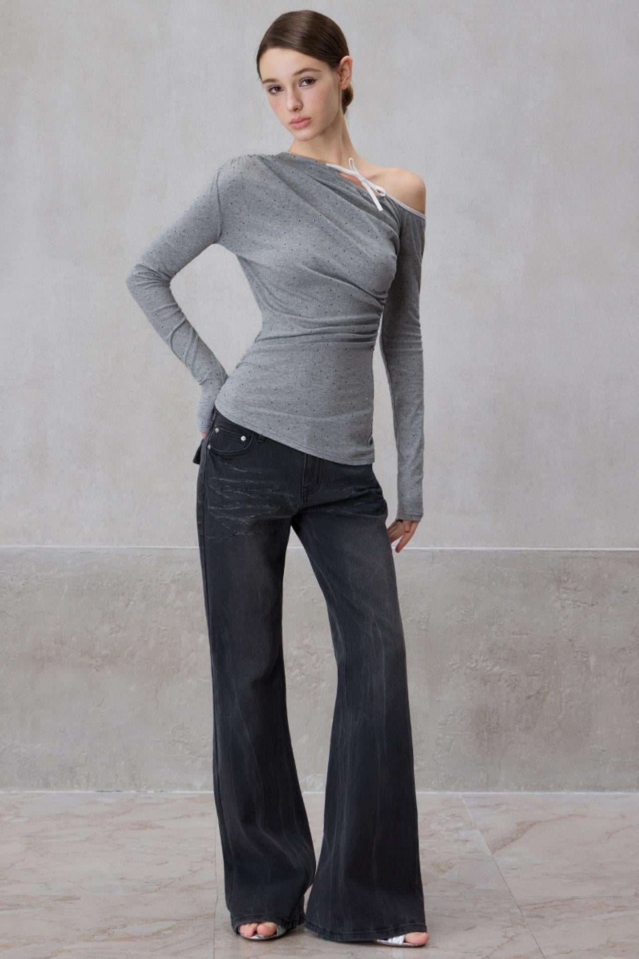 Woman wearing a gray long-sleeve top and dark jeans against a plain background