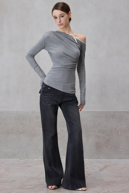 Woman wearing a gray long-sleeve top and dark jeans against a plain background