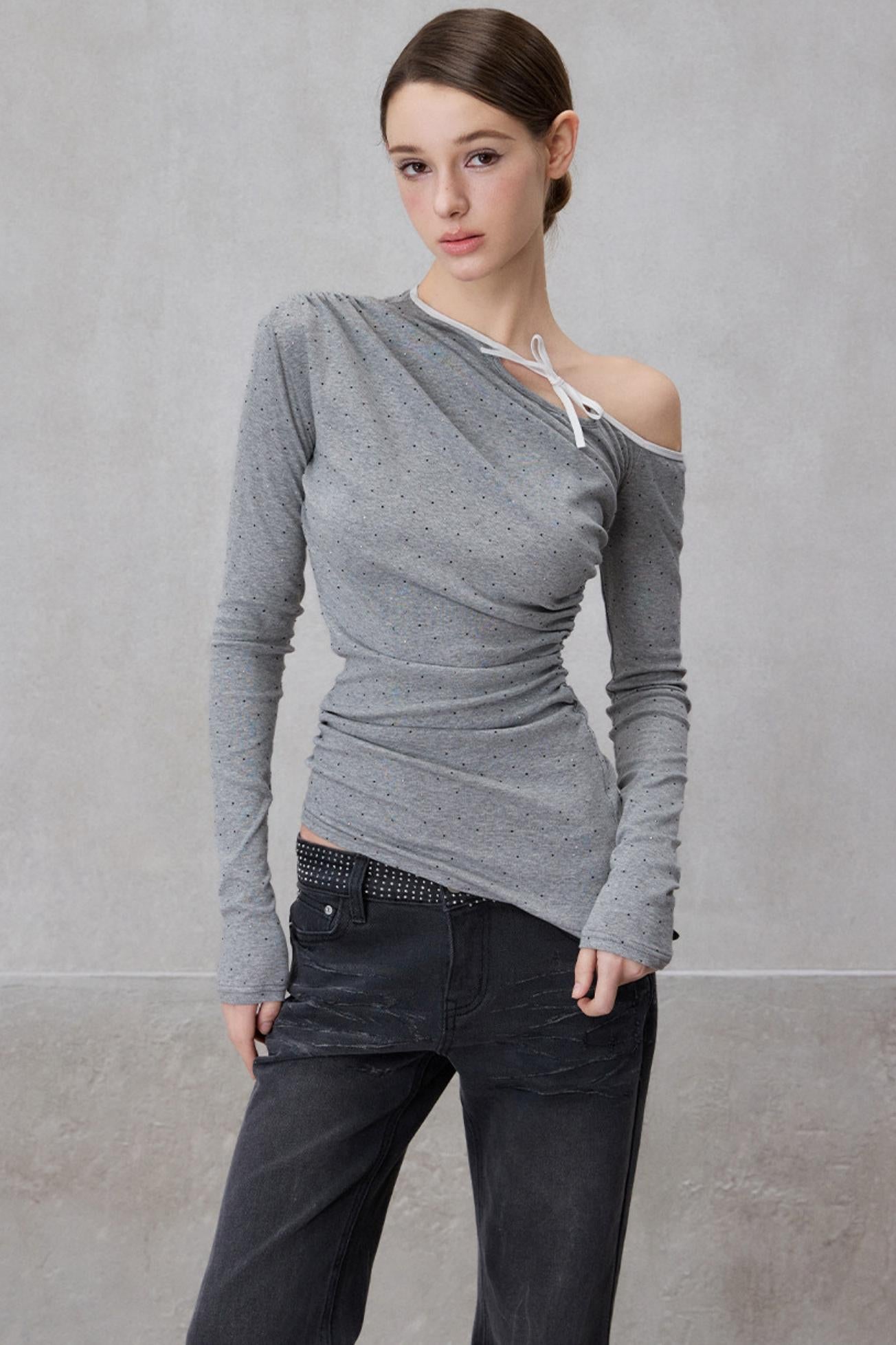 Woman wearing a gray off-shoulder top and dark pants against a plain background