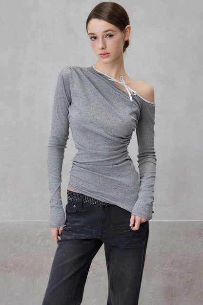 Woman wearing a gray off-shoulder top and dark pants against a plain background