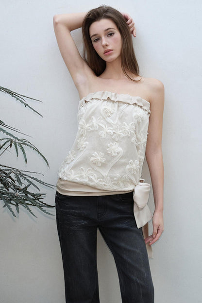 Woman wearing a strapless floral top and dark pants against a light background